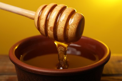 Photo of Pouring honey from dipper into bowl at table against golden background, closeup