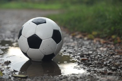 Leather soccer ball in puddle outdoors, space for text
