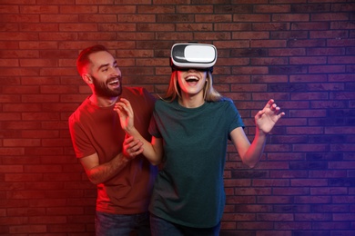 Photo of Emotional woman playing video games with VR headset and happy man near brick wall