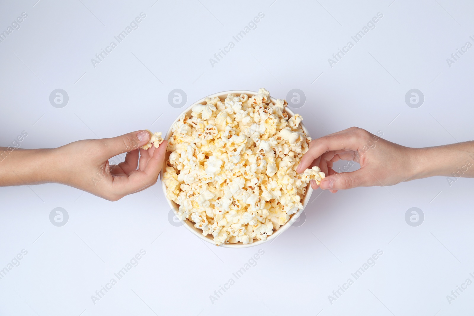 Photo of Women eating tasty popcorn from paper bucket on white background, top view