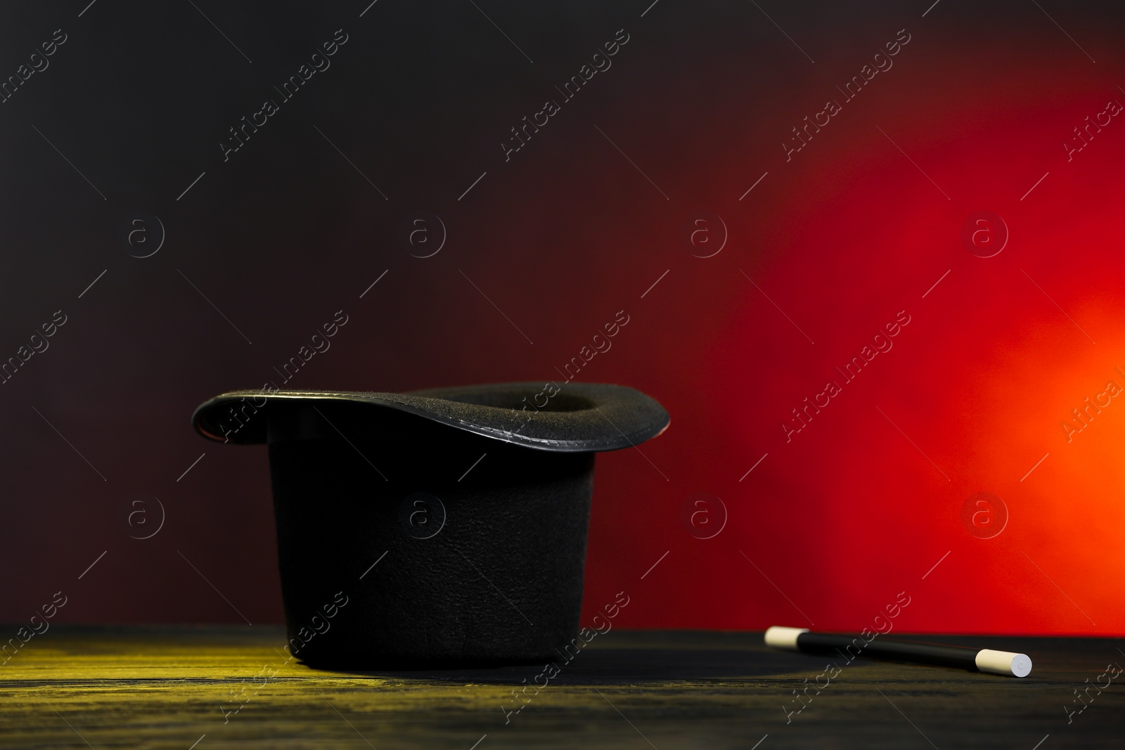 Photo of Magician's hat and wand on wooden table against dark background, space for text