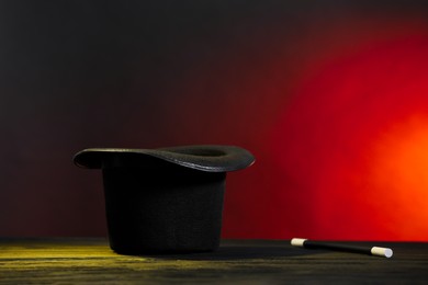 Photo of Magician's hat and wand on wooden table against dark background, space for text