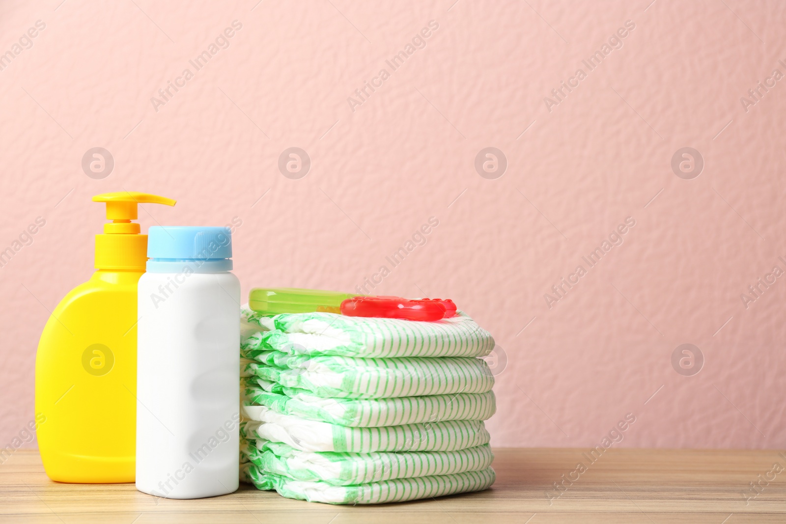 Photo of Stack of diapers, toiletries and teether on table against color background, space for text. Baby accessories