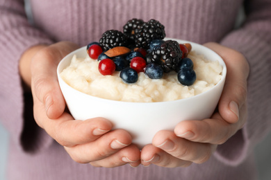 Woman holding bowl of delicious rice pudding with berries, closeup