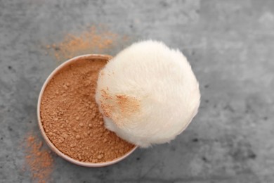 Face powder and puff applicator on grey textured table, top view. Space for text