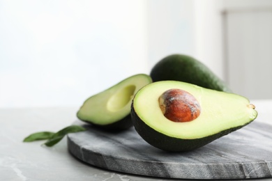 Halves of delicious ripe avocado on table against light background