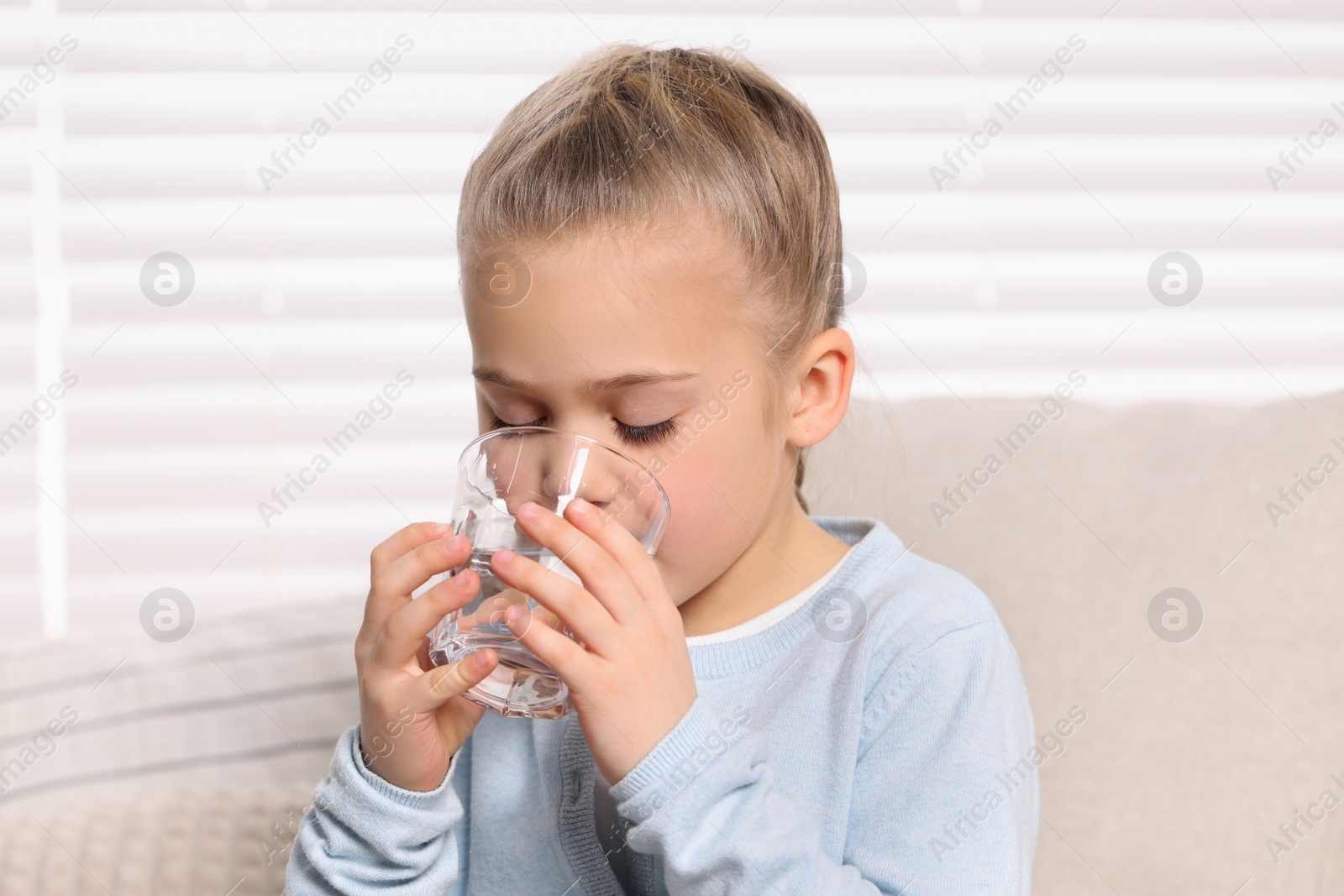 Photo of Cute little girl drinking fresh water from glass indoors