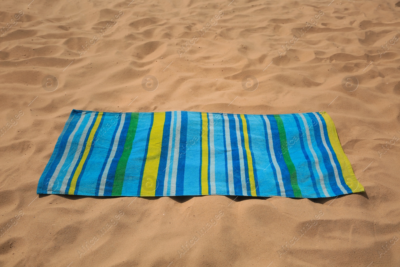 Photo of Soft bright striped beach towel on sand