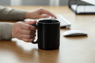 Woman with black ceramic mug at workplace, closeup