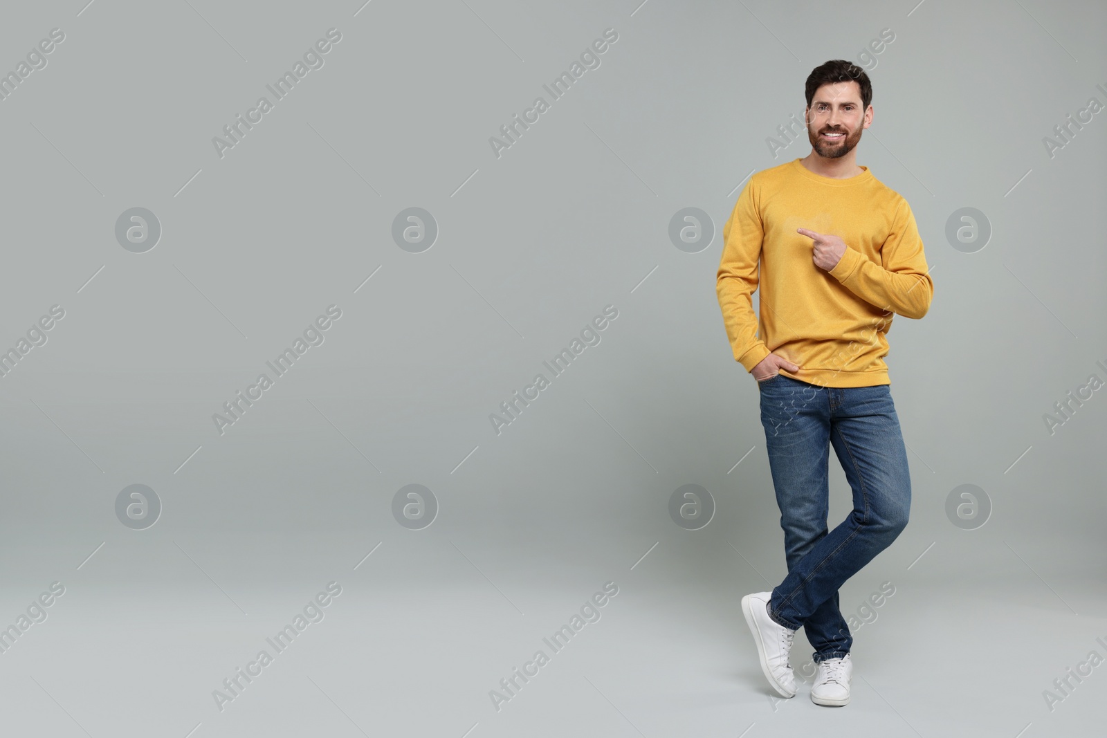 Photo of Smiling man pointing at something on grey background. Space for text