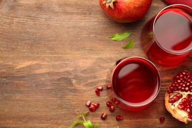 Photo of Tasty pomegranate juice in glasses and fresh fruits on wooden table, flat lay. Space for text
