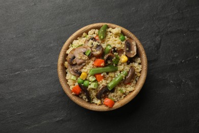 Photo of Delicious bulgur with vegetables and mushrooms in bowl on black table, top view