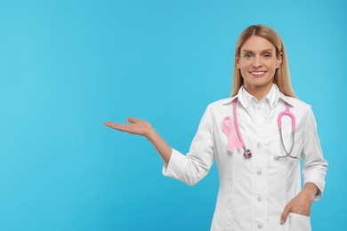 Photo of Doctor with pink ribbon and stethoscope on light blue background, space for text. Breast cancer awareness