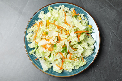 Photo of Plate of fresh cabbage salad with carrot on grey table, top view