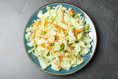 Plate of fresh cabbage salad with carrot on grey table, top view