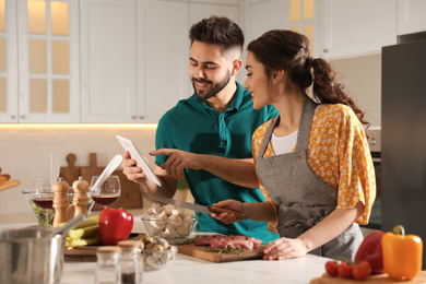 Photo of Lovely young couple with tablet cooking together in kitchen