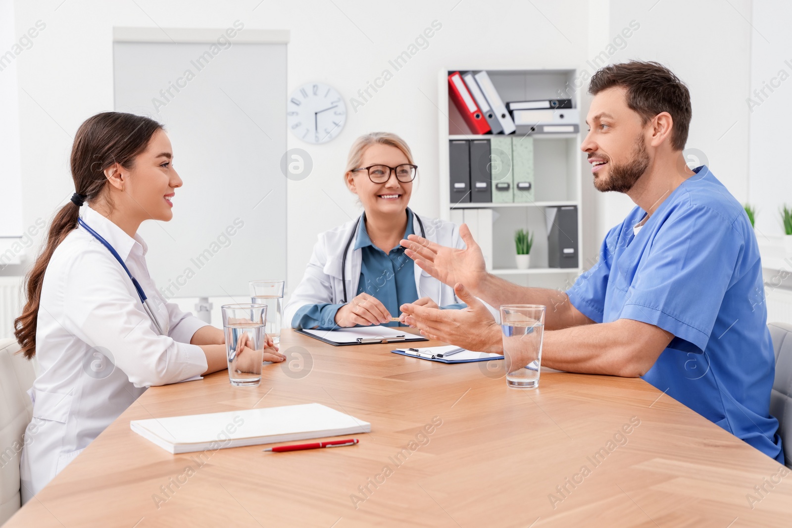 Photo of Medical conference. Team of doctors having discussion at wooden table in clinic