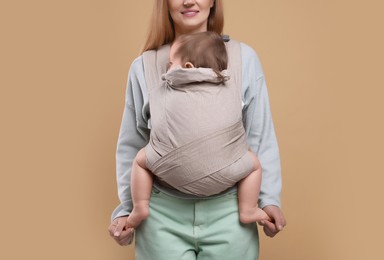 Photo of Mother holding her child in sling (baby carrier) on light brown background, closeup