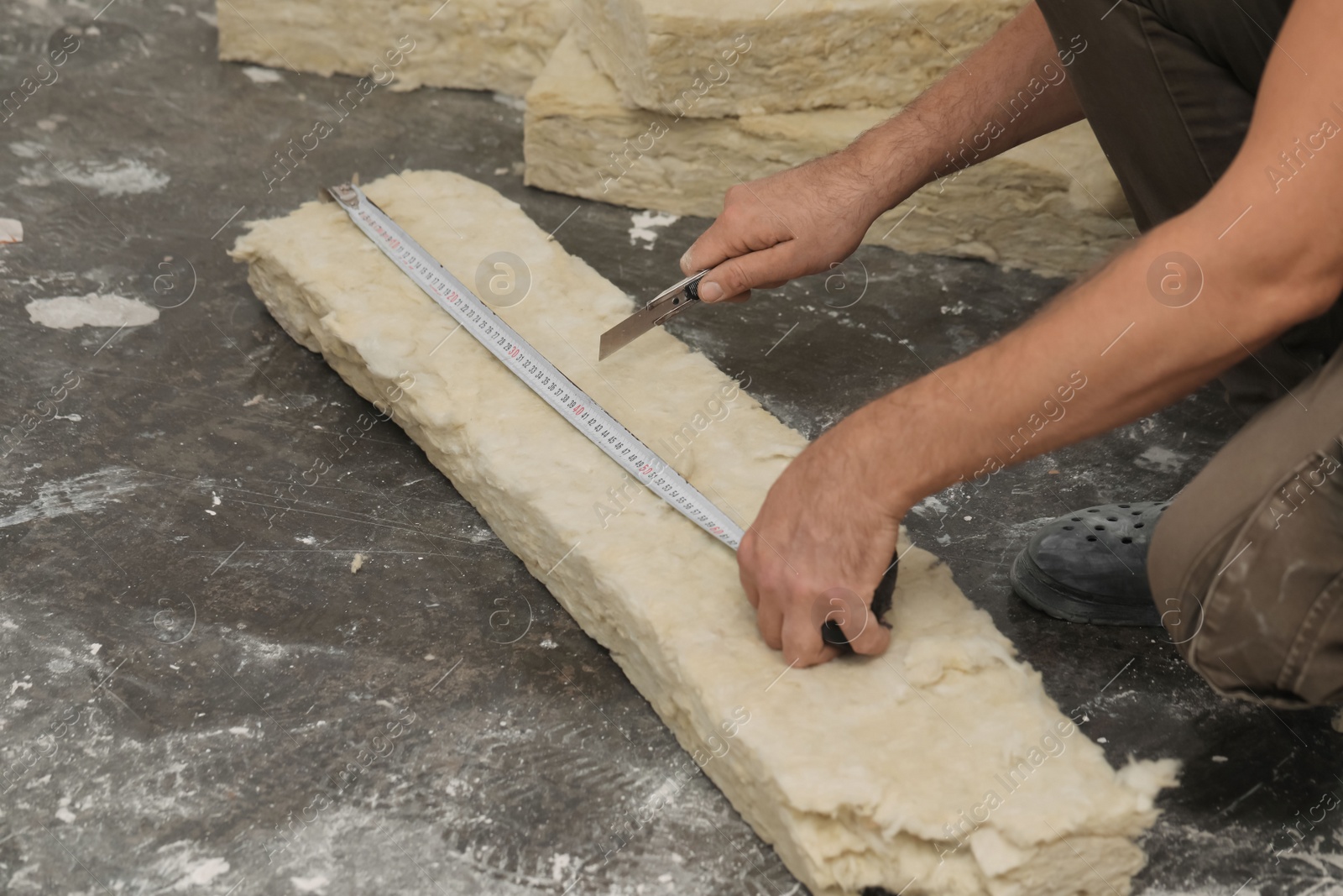 Photo of Worker measuring and cutting insulation material indoors, closeup