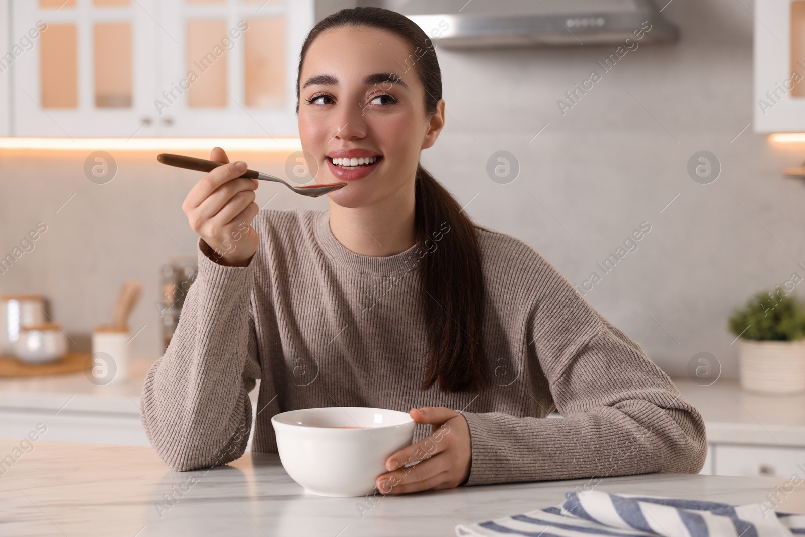 Photo of Smiling woman eating tasty soup at white marble table in kitchen