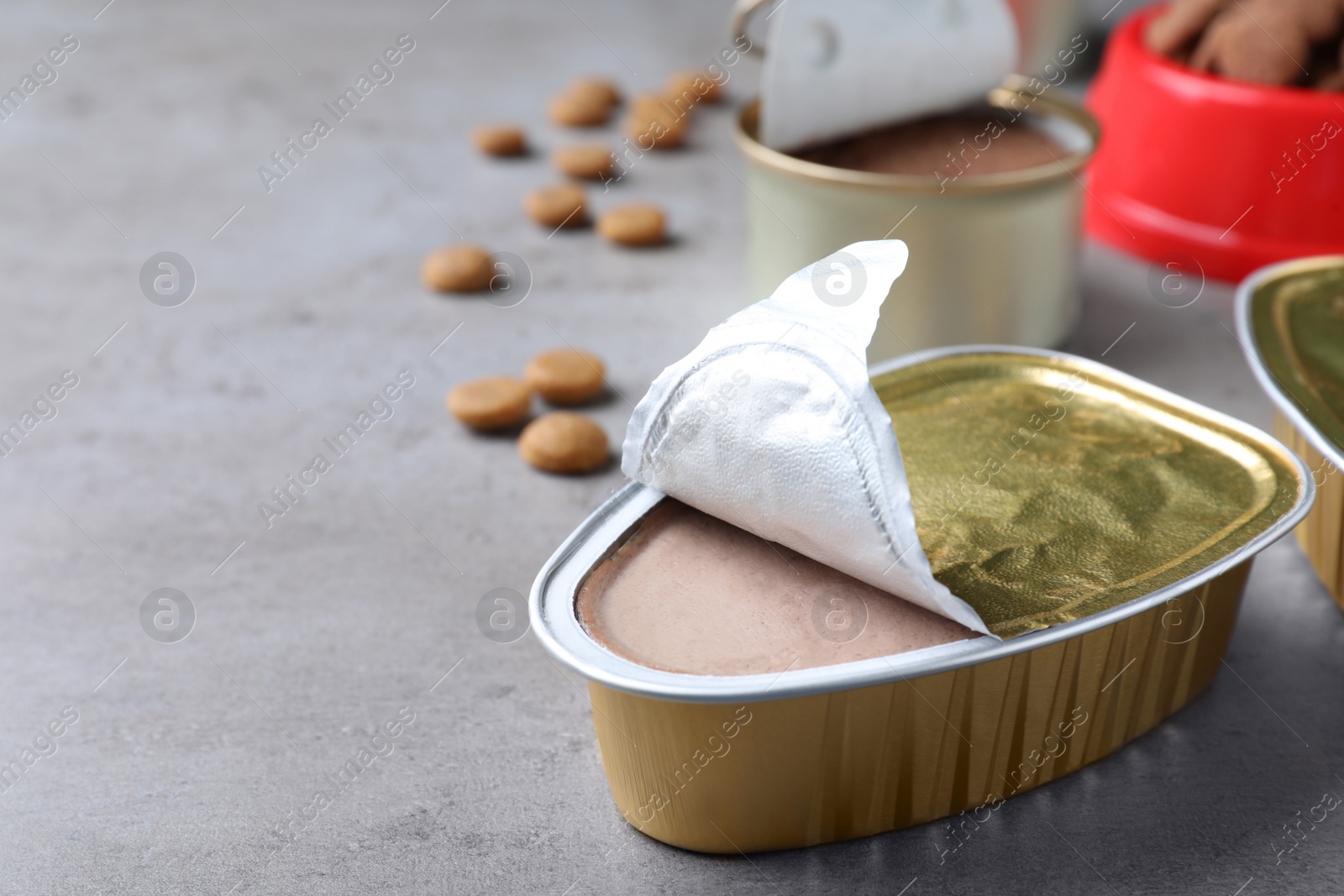 Photo of Open package of wet pet food on grey table. Space for text