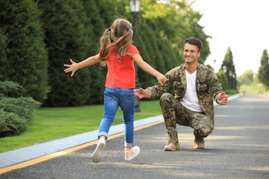 Little daughter running to her father in military uniform at sunny park