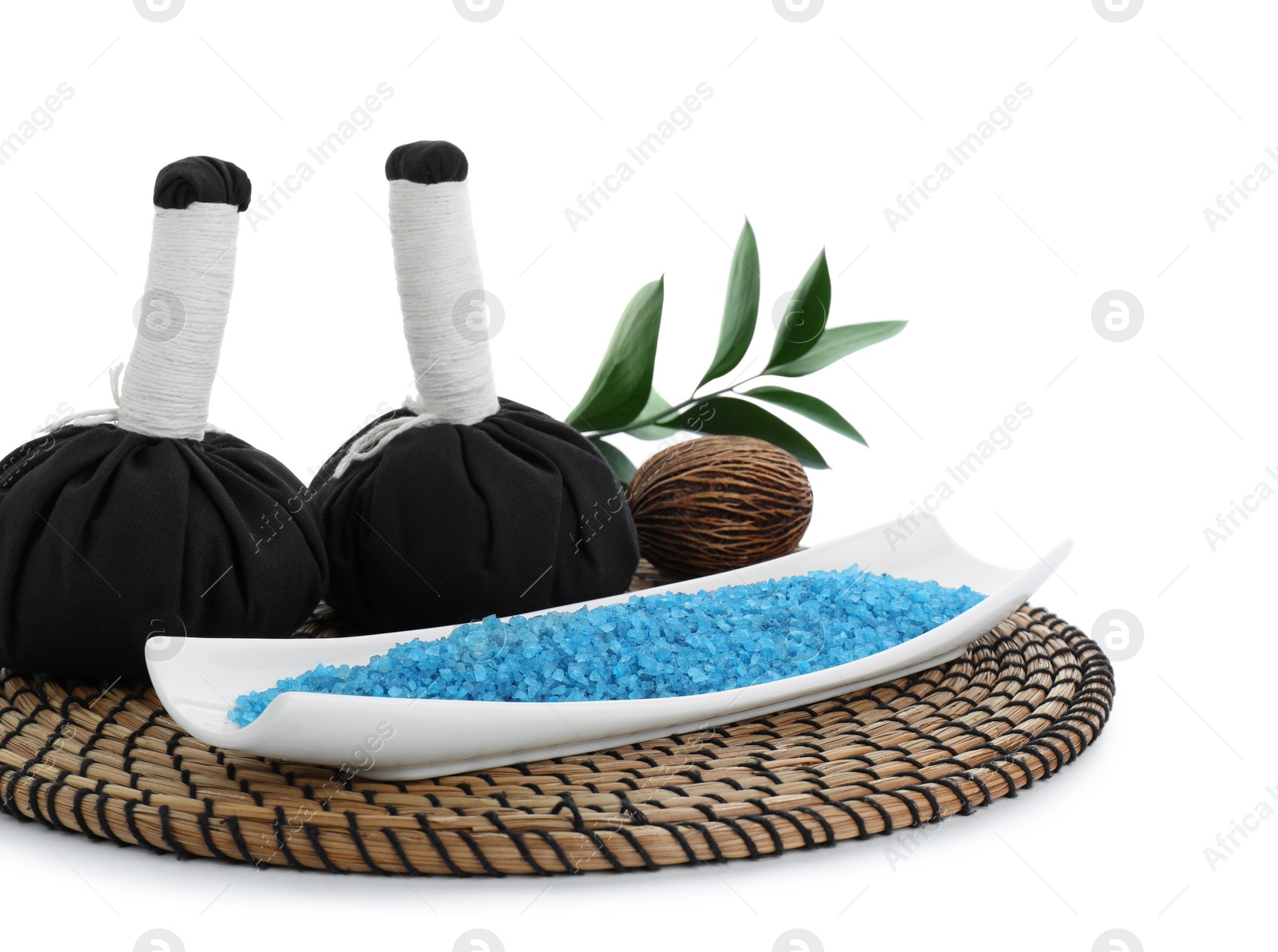 Photo of Wicker mat with blue sea salt and herbal bags isolated on white