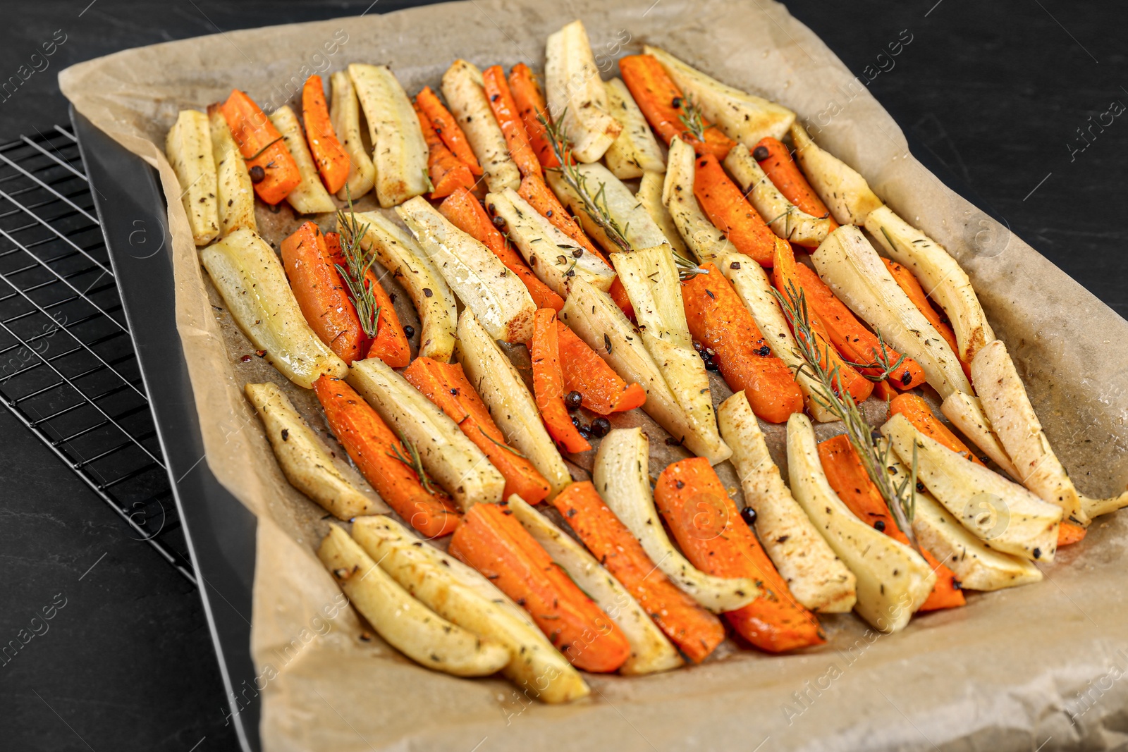 Photo of Tray with parchment, baked parsnips and carrots on black table