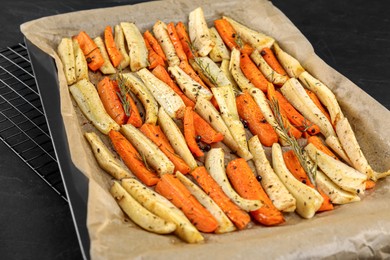 Tray with parchment, baked parsnips and carrots on black table