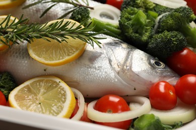 Photo of Raw fish with vegetables and lemon in baking dish, closeup