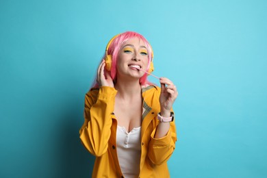 Photo of Fashionable young woman in pink wig with headphones chewing bubblegum on yellow background