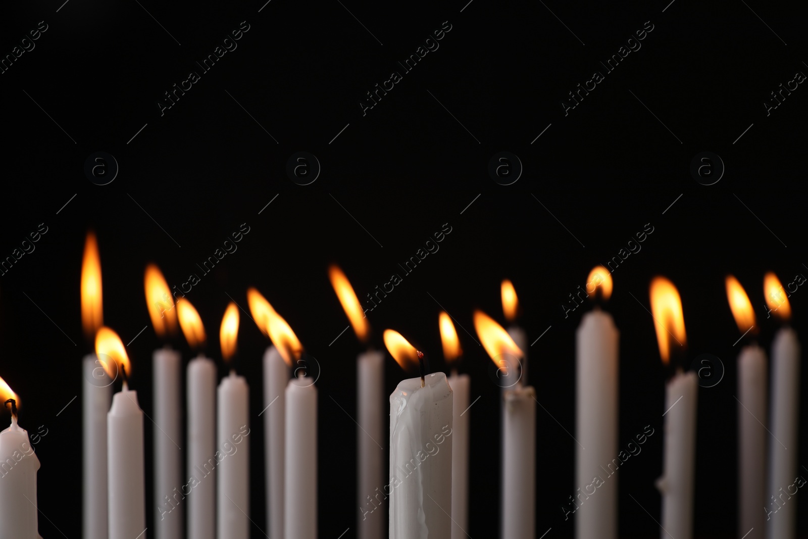 Photo of Many burning church candles on black background