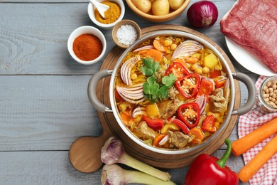 Photo of Delicious vegetable soup with meat in saucepan and ingredients on grey wooden table, flat lay. Space for text