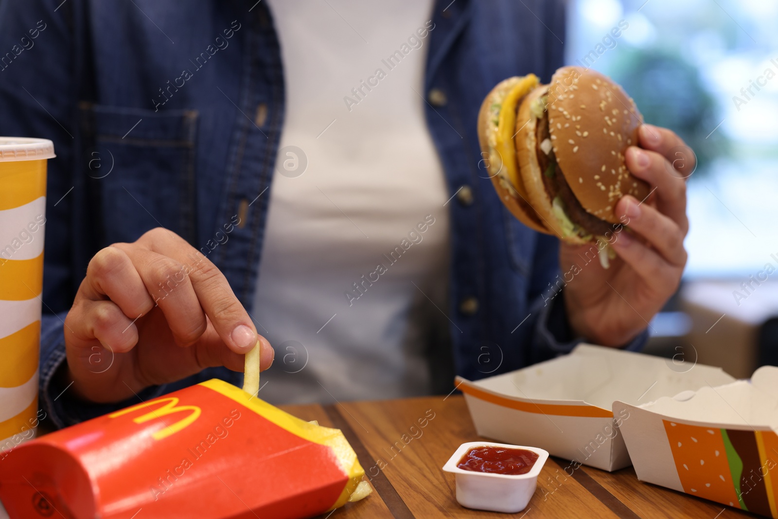 Photo of Lviv, Ukraine - October 9, 2023: Woman with McDonald's menu at wooden table in restaurant, closeup