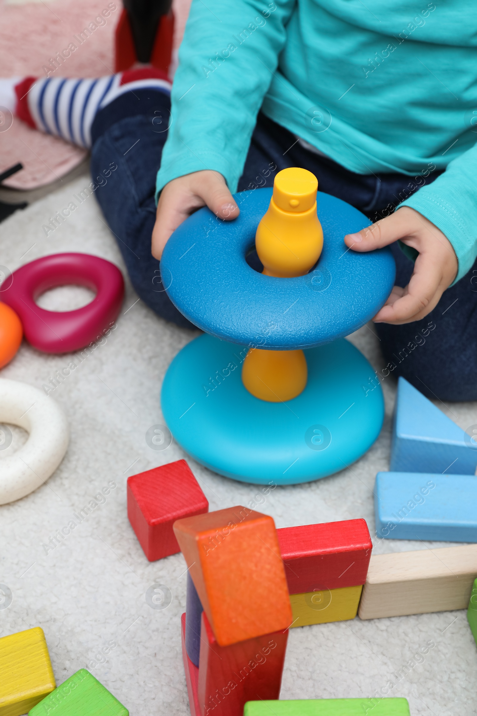 Photo of Little child playing with stacking toy on carpet, closeup