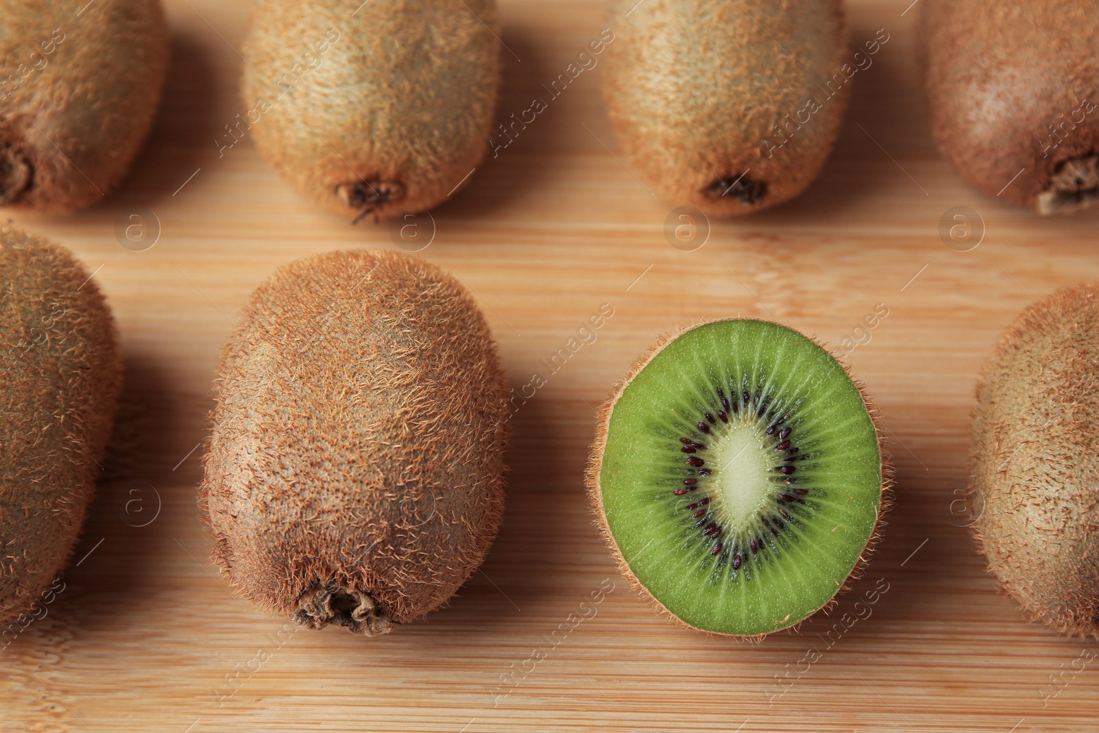 Photo of Wooden board with whole kiwis and cut one, top view