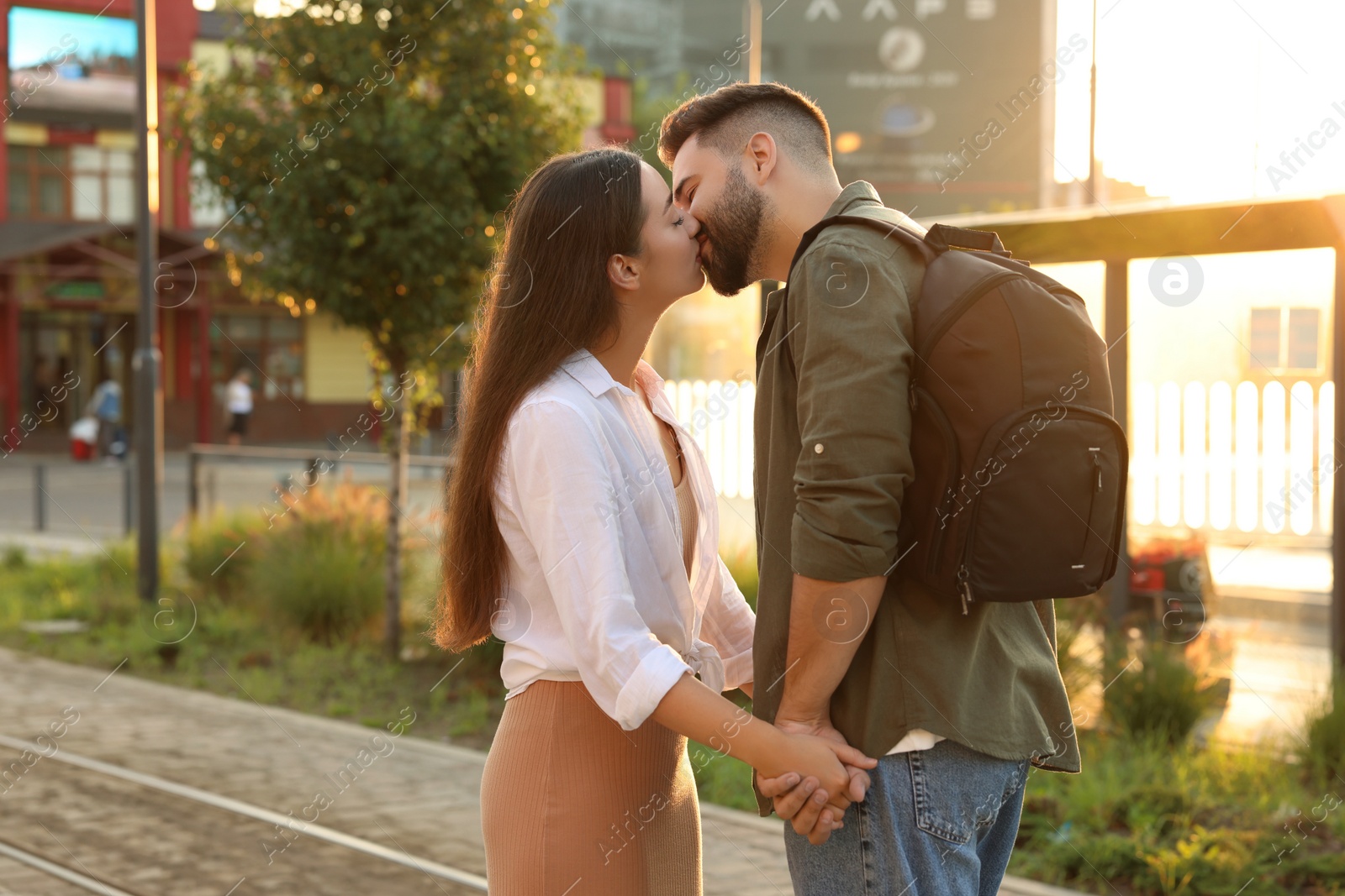 Photo of Long-distance relationship. Man with backpack kissing his girlfriend at railway station outdoors