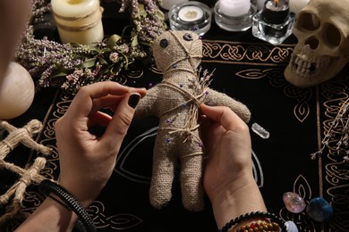 Photo of Woman stabbing voodoo doll with needle at table, closeup. Curse ceremony