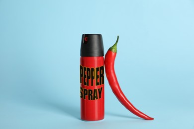 Bottle of gas spray and fresh chili pepper on light blue background