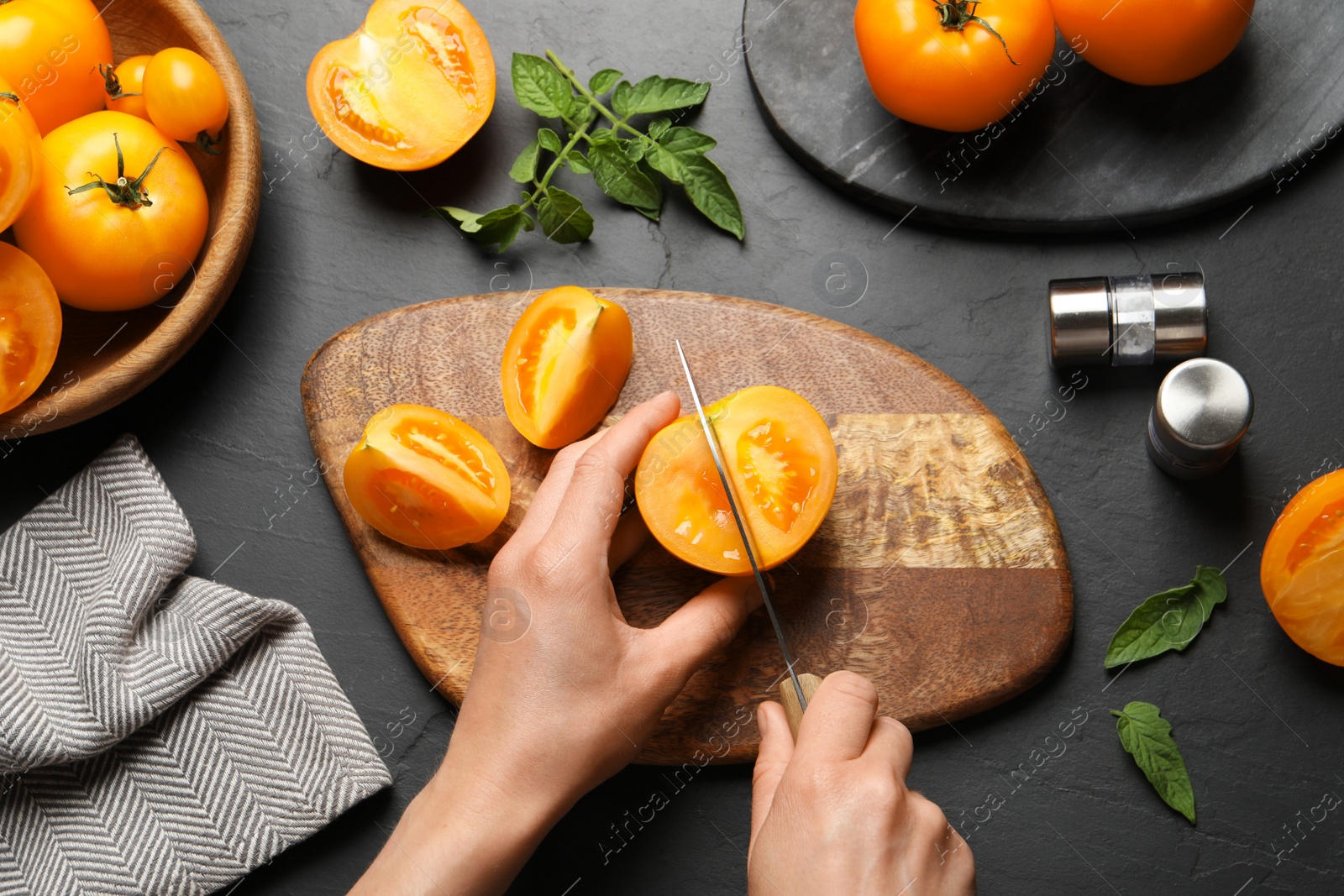 Photo of Woman cutting fresh ripe yellow tomato at black table, top view