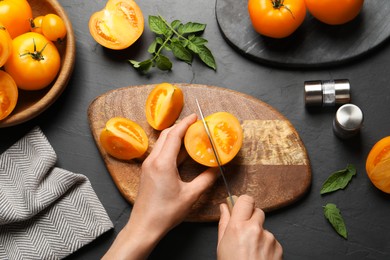 Woman cutting fresh ripe yellow tomato at black table, top view