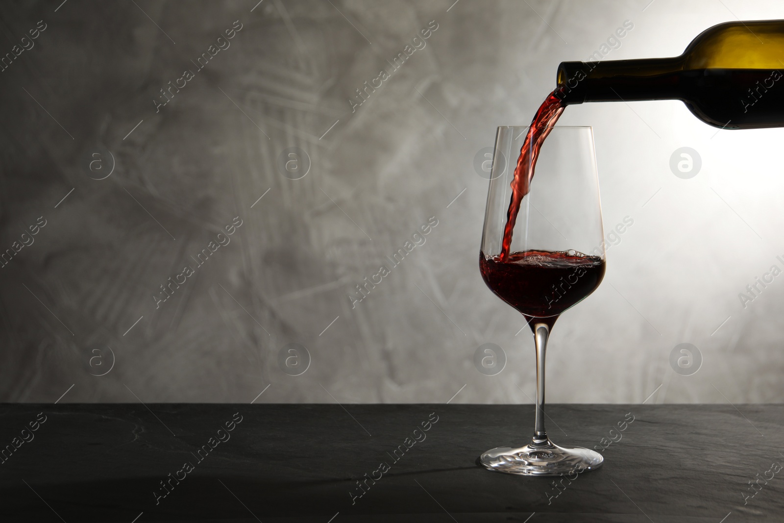 Photo of Pouring red wine from bottle into glass on table. Space for text