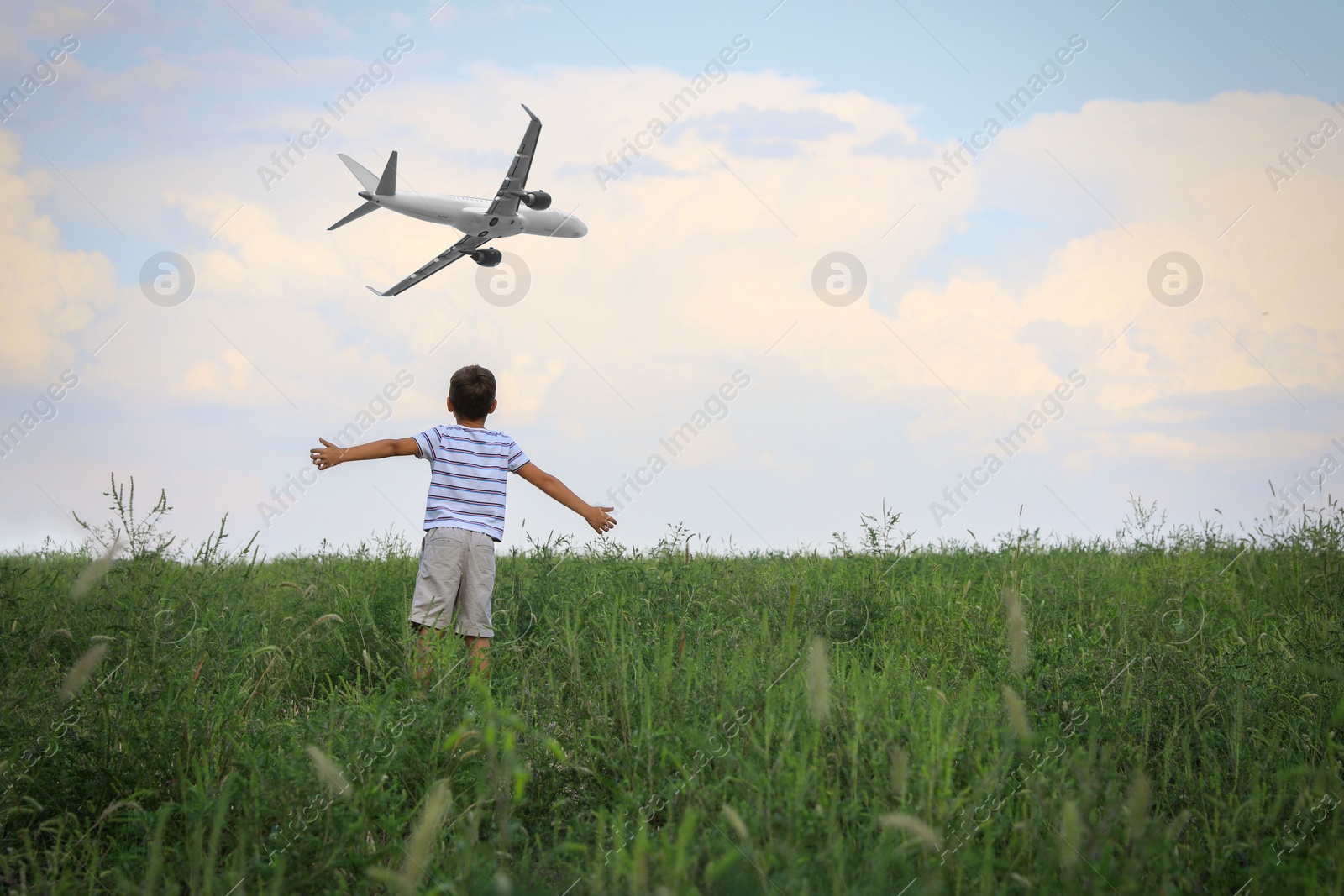 Image of Boy in green field looking at airplane flying in sky, back view