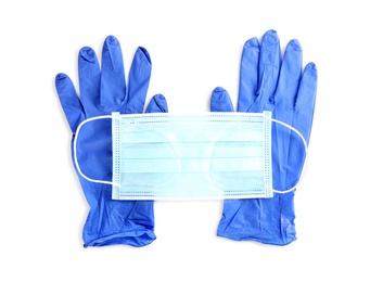 Medical gloves and protective face mask on white background, top view