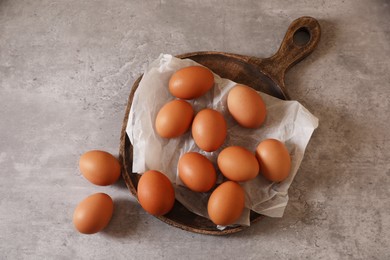 Chicken eggs, wooden board and parchment paper on grey table, flat lay