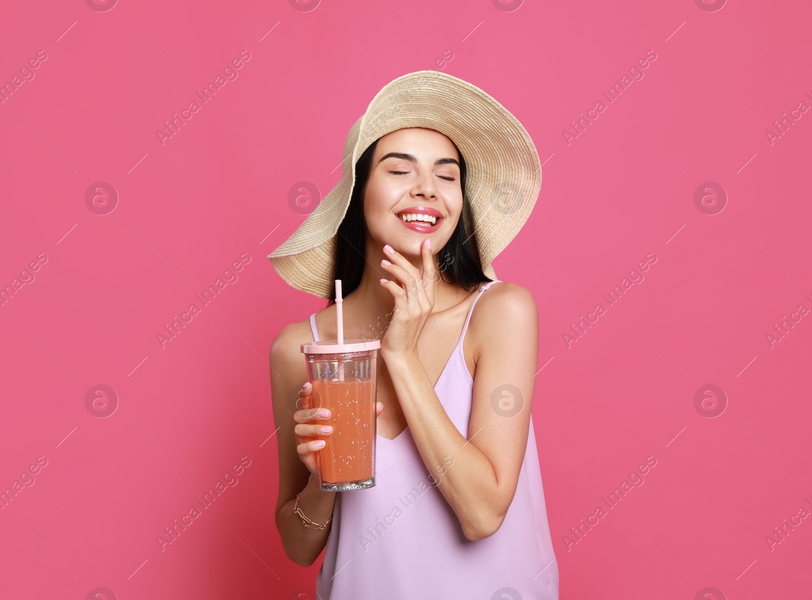 Photo of Beautiful young woman with straw hat and glass of refreshing drink on pink background