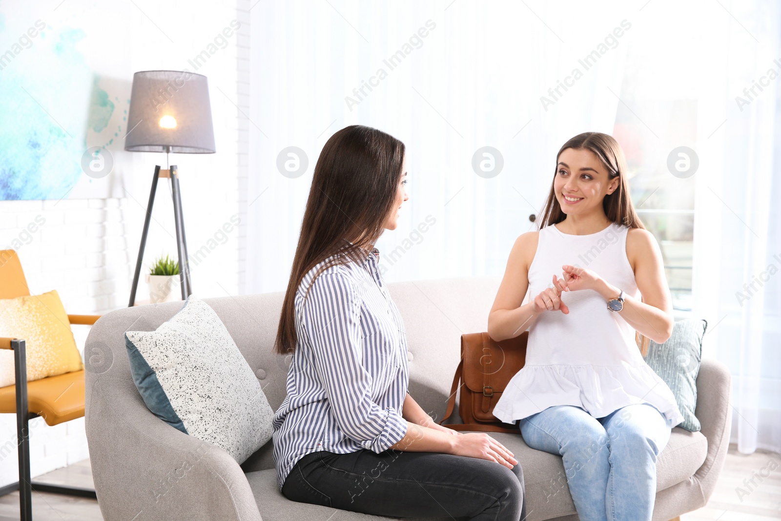 Photo of Hearing impaired friends using sign language for communication on sofa in living room