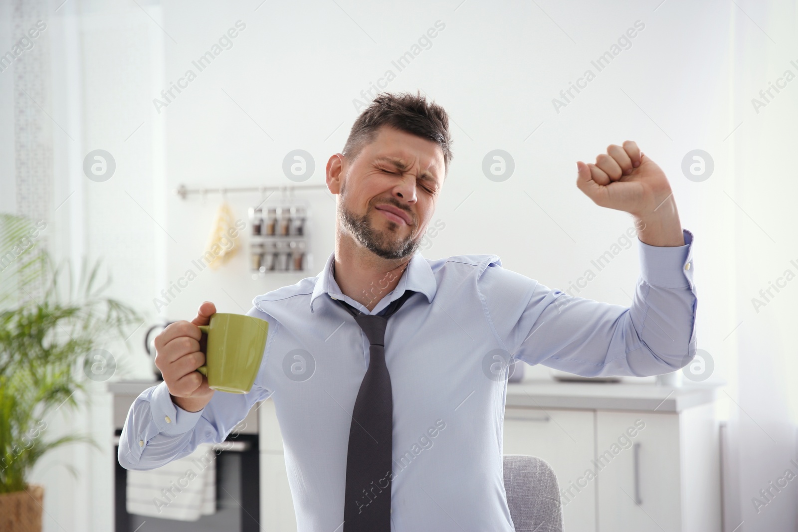 Photo of Sleepy man with cup of drink at home in morning