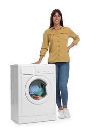 Beautiful woman near washing machine with laundry on white background