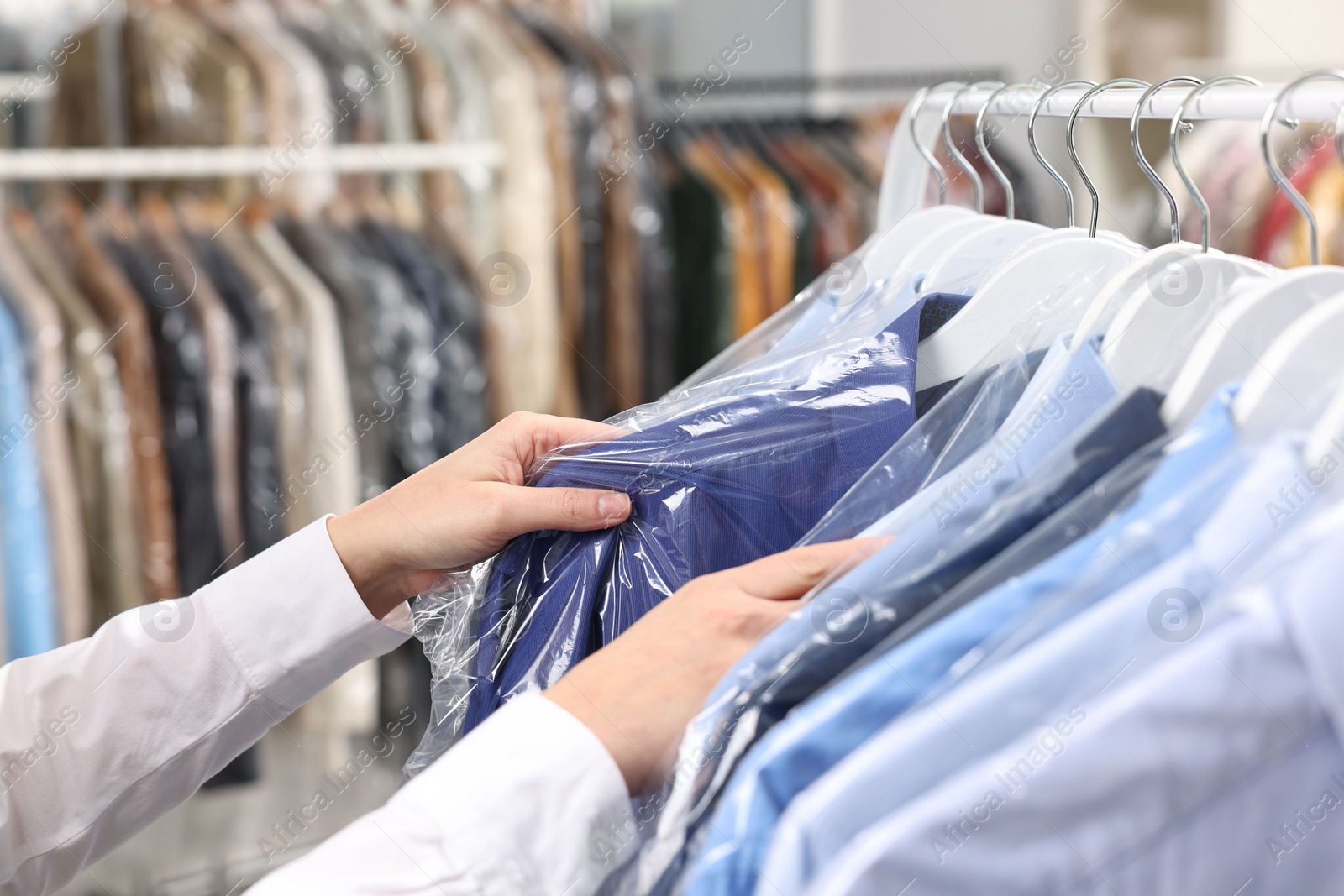 Photo of Dry-cleaning service. Woman taking shirt in plastic bag from rack indoors, closeup